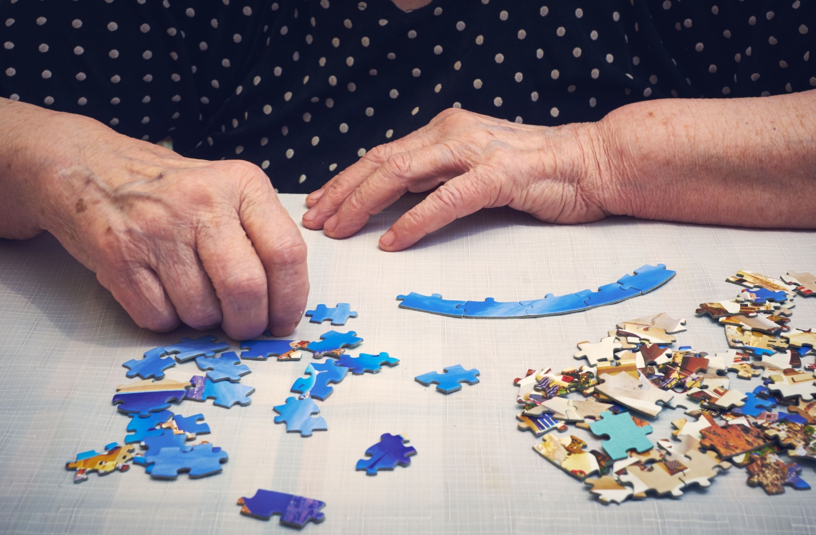 A close-up image of an older adult assembling blue pieces of a puzzle of a city skyline