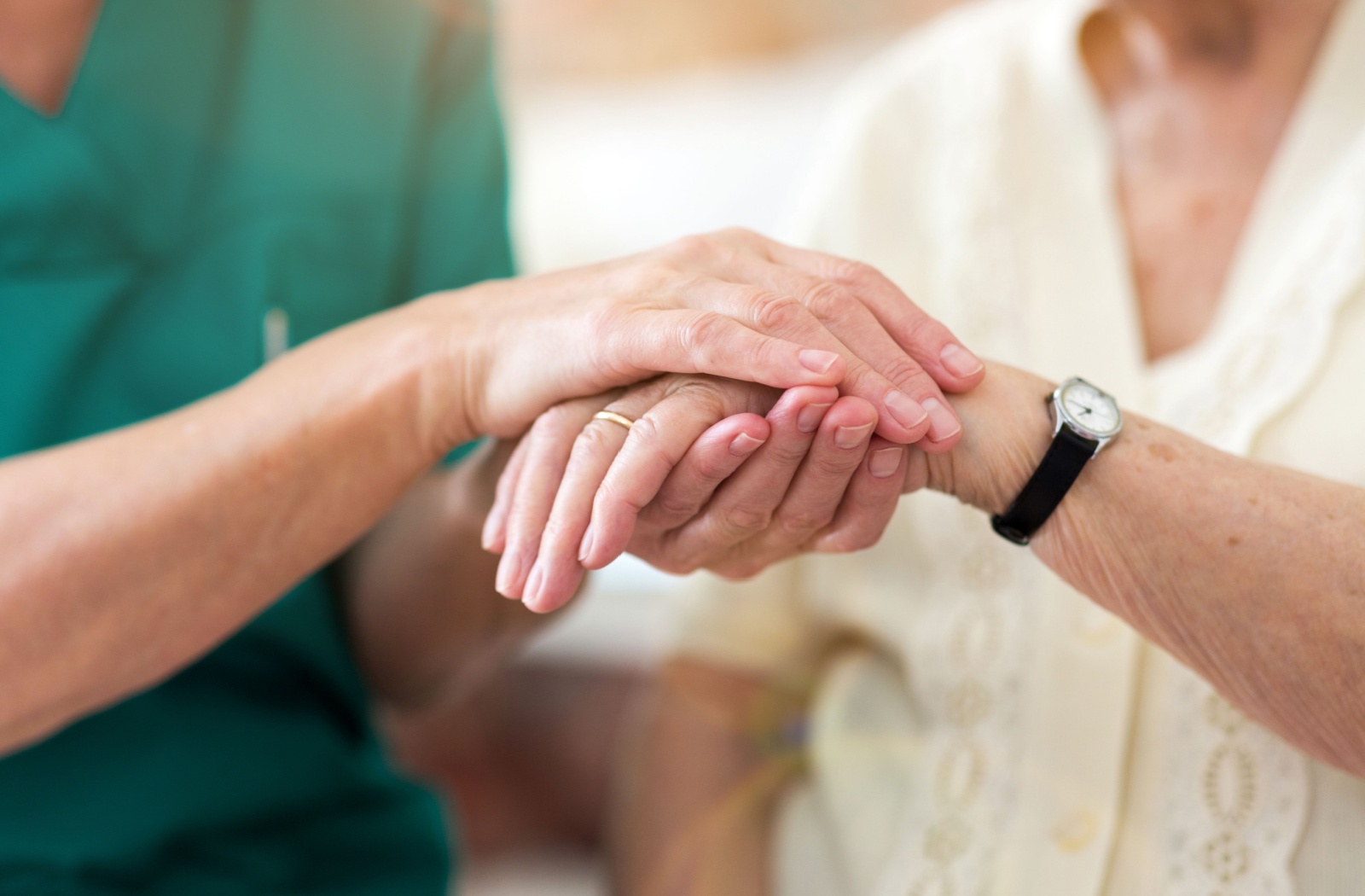 A caregiver holds the hand of a memory care resident.