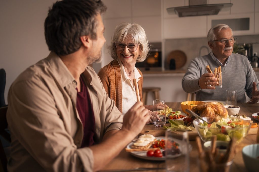 Multigenerational family laughing and sharing a festive, healthy meal at the dining table, enjoying conversation, connection, and warm, casual togetherness at home
