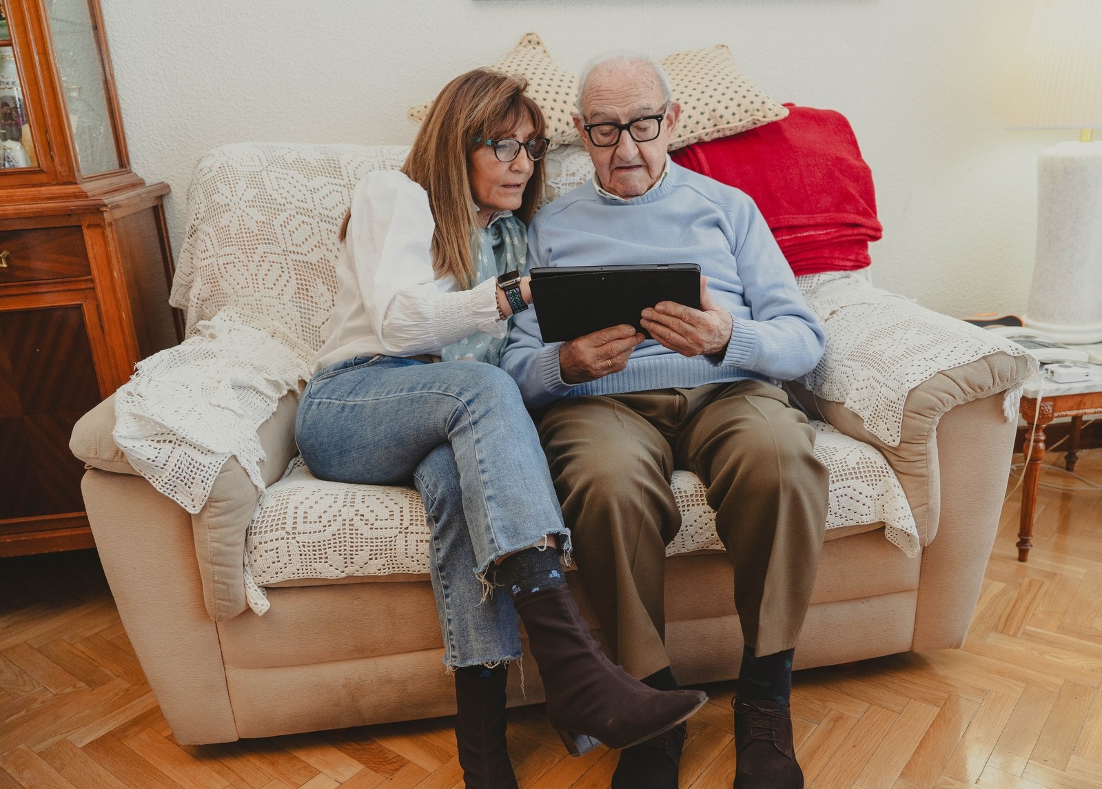 Adult daughter helping senior father navigate a digital tablet on a living room couch