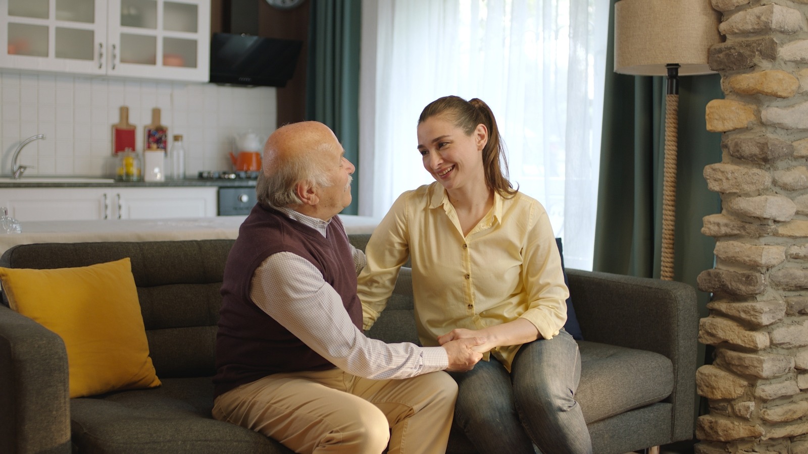 Adult daughter and elderly father sitting on a sofa, enjoying friendly conversation in a senior living community.